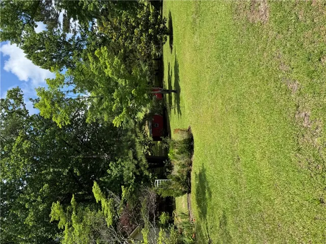 A verdant expanse of lawn provides a tranquil backdrop for the secluded red shed nestled among mature trees.