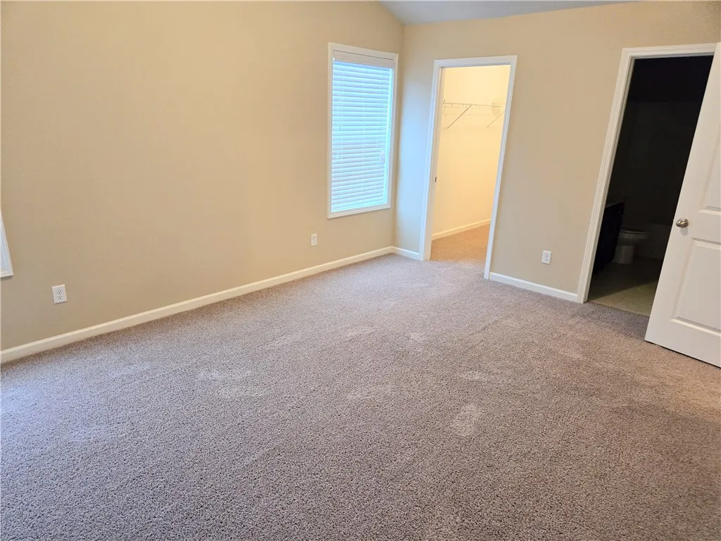 A well-lit room offers soft carpeting and convenient access to a walk-in closet and a private bathroom.