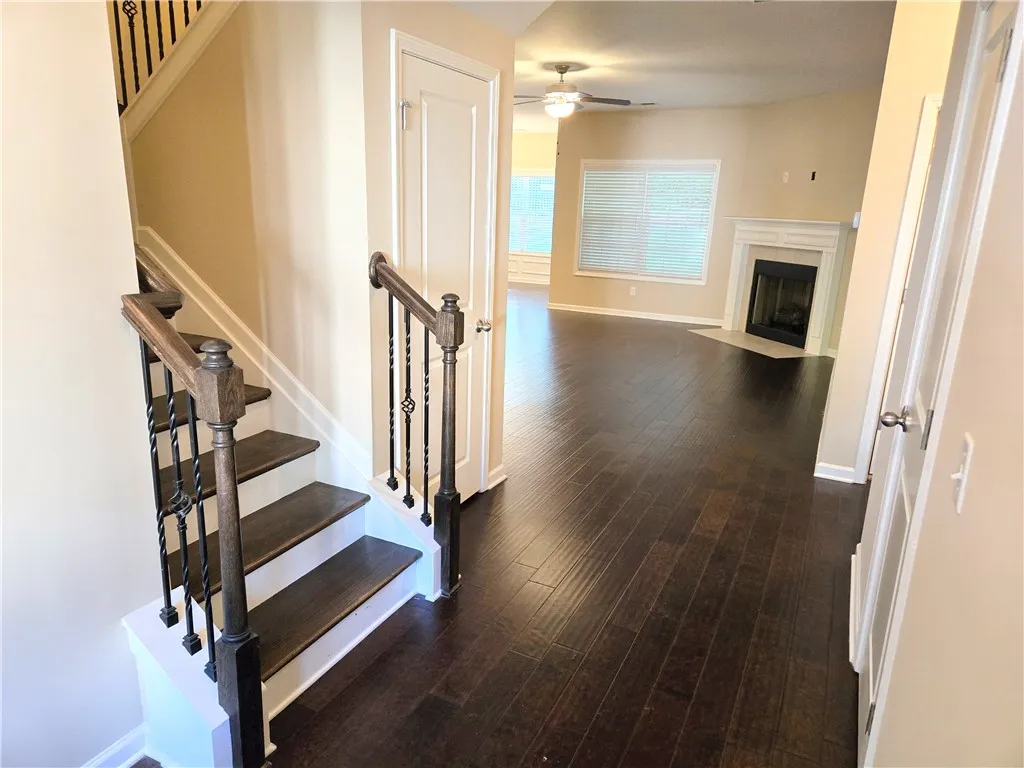 Rich hardwood flooring guides you from the elegant staircase into a well-lit living space with a classic fireplace.