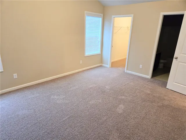 A well-lit room offers soft carpeting and convenient access to a walk-in closet and a private bathroom.