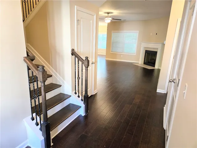 Rich hardwood flooring guides you from the elegant staircase into a well-lit living space with a classic fireplace.