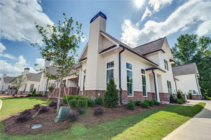 Crisp white siding complements a brick foundation, accented by dark window frames and lush, new landscaping.
