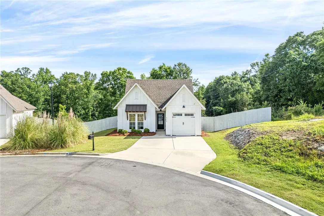 A charming single-story residence boasts crisp white siding and a well-manicured lawn with an inviting driveway leading to the garage.