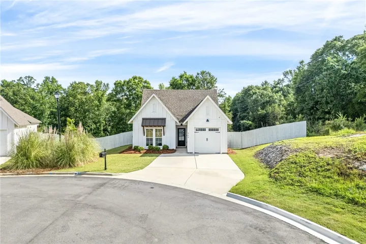 A charming single-story residence boasts crisp white siding and a well-manicured lawn with an inviting driveway leading to the garage.