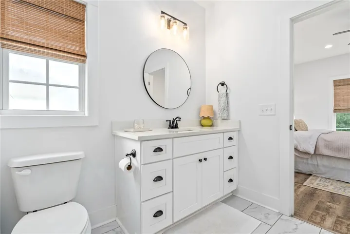 White vanity with a round mirror and overhead lighting creates a fresh bathroom aesthetic.