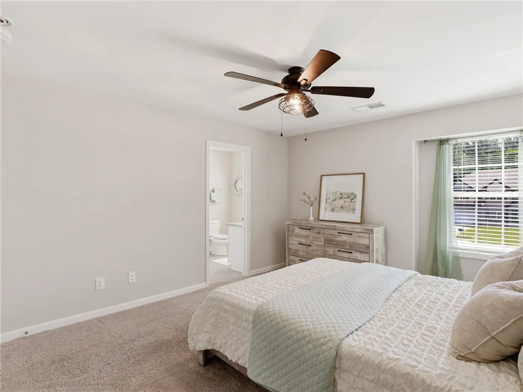 An inviting sleeping space with soft carpet flooring and a refreshing ceiling fan.