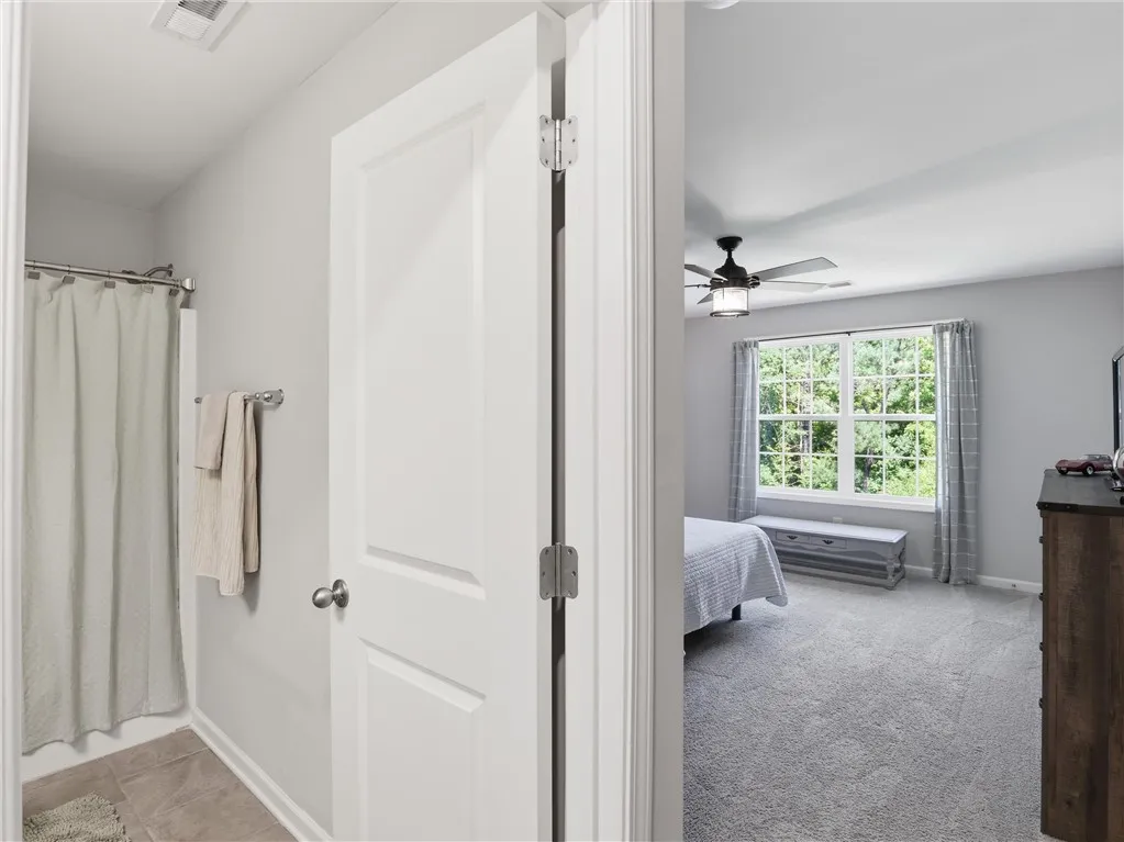 A well-lit bedroom with plush carpeting offers views of lush greenery.