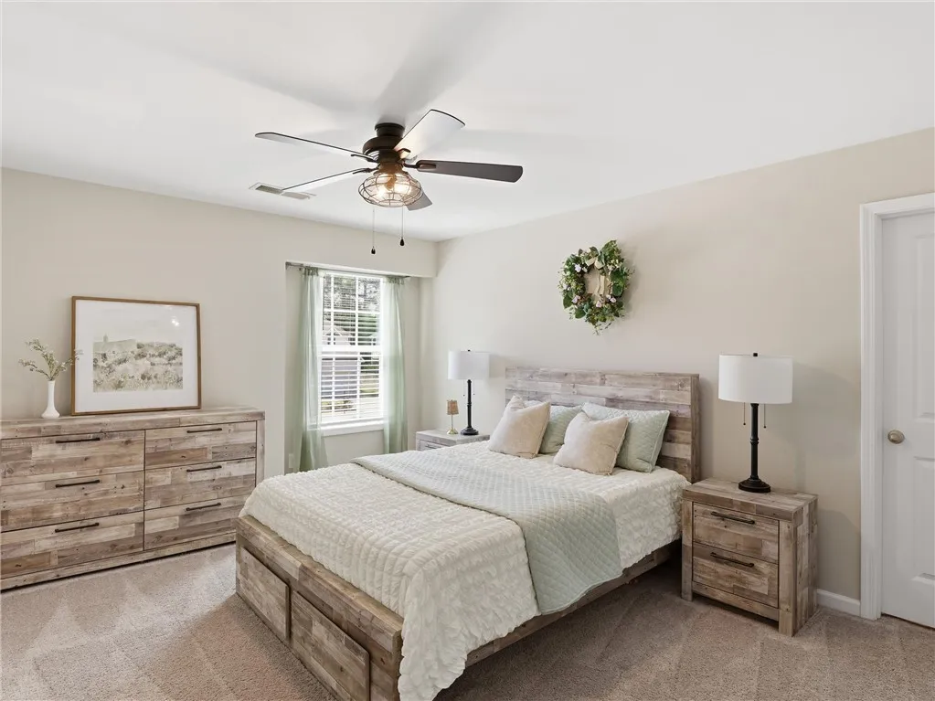 Well-lit bedroom with carpeted flooring features a ceiling fan, a window, and a door for convenient access.