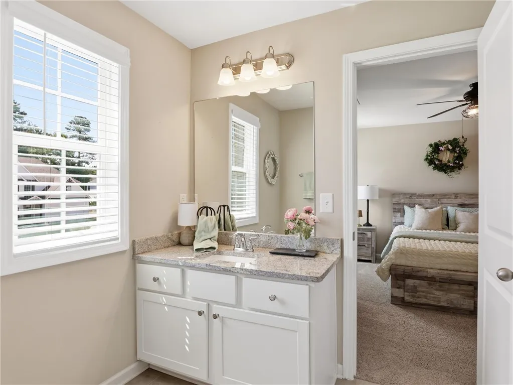 A window-lit bathroom vanity with granite counters offers a clear view into an adjoining bedroom.