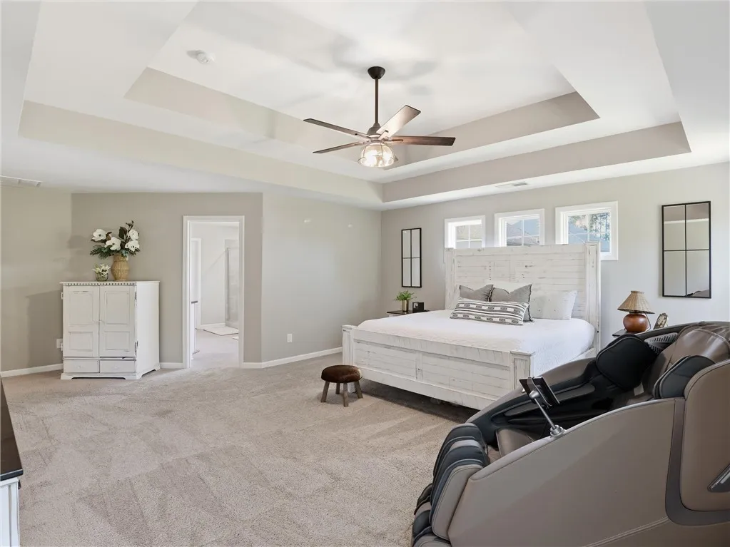 A spacious primary bedroom features a unique tray ceiling, carpeted floor, and sun-filled windows.