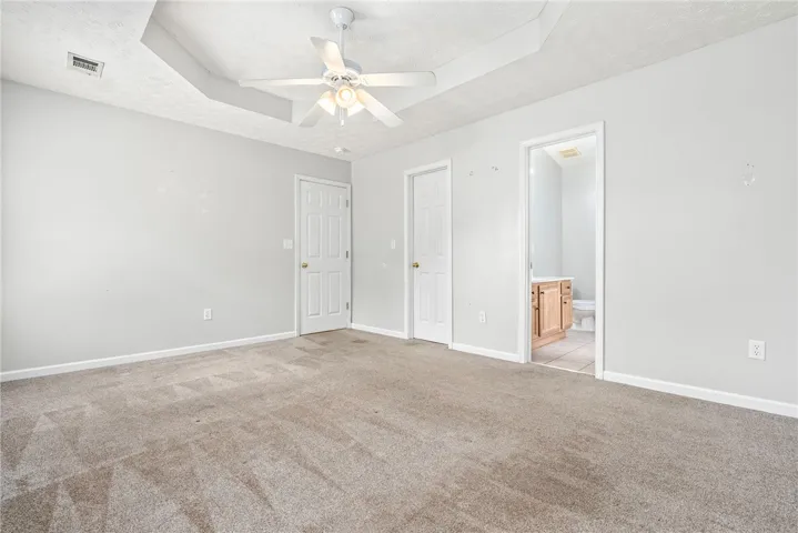 A spacious primary features a tray ceiling with a prominent ceiling fan and neutral carpeting.