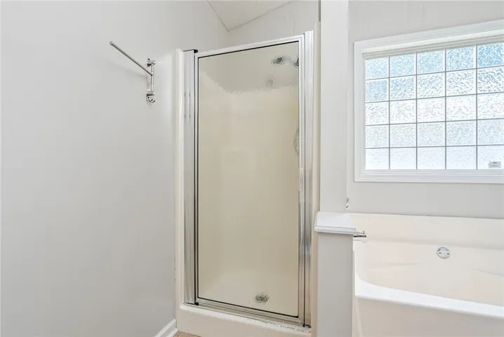 A well-lit primary bathroom featuring a walk-in shower and a soaking tub beneath a privacy window.