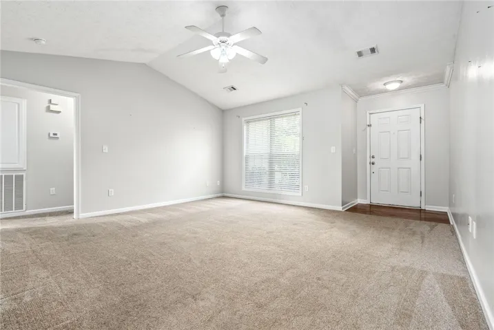 A spacious common area offers plush carpeting, a vaulted ceiling, and ample natural light from a well-sized window.
