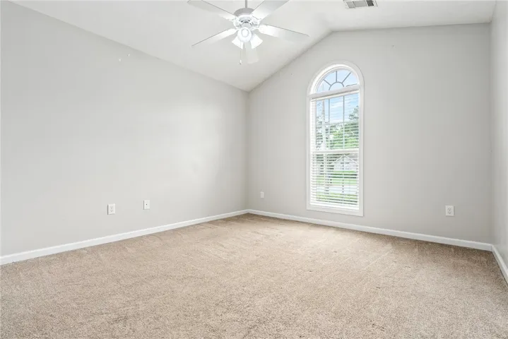 A graceful arched window illuminates this comfortable room, featuring vaulted ceilings and soft carpet.