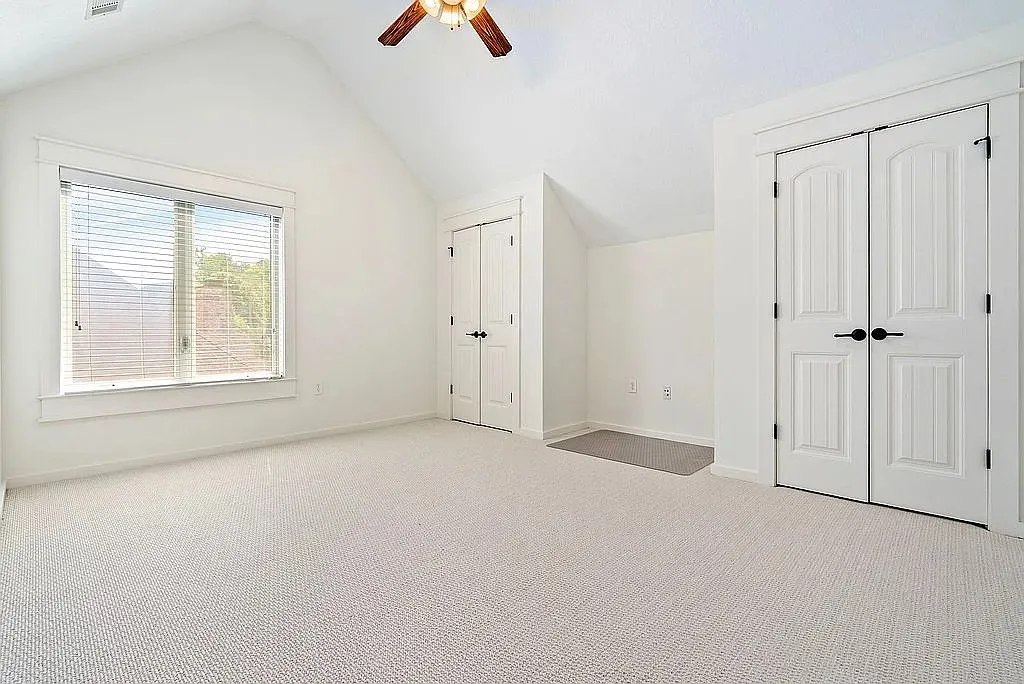 A spacious room features a vaulted ceiling, soft carpet, and a broad window for ample natural light.