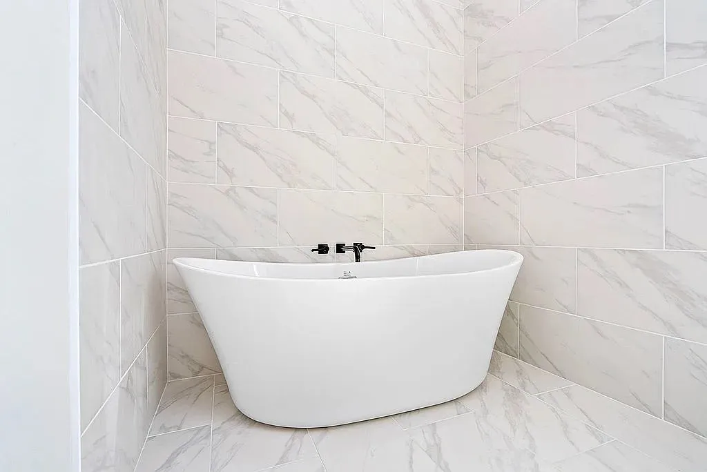 A freestanding soaking tub nestled in a serene alcove, surrounded by chic marble-patterned tile.