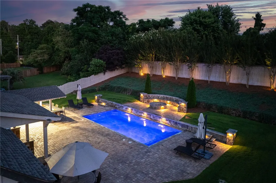 An illuminated backyard oasis featuring a pristine pool with water features and a cozy fire pit.
