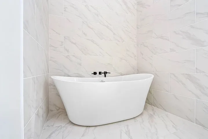 A freestanding soaking tub nestled in a serene alcove, surrounded by chic marble-patterned tile.