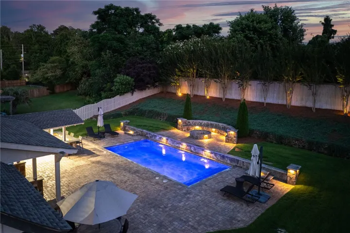 An illuminated backyard oasis featuring a pristine pool with water features and a cozy fire pit.