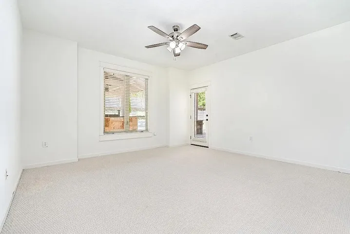 A spacious room offers comfortable carpeted flooring and a ceiling fan, with a window and a glass-paneled door for light.