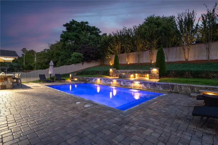 An illuminated backyard oasis with a pristine pool and charming stone waterfall features.