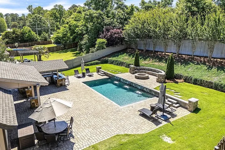 An inviting backyard oasis offers a sparkling pool, integrated fire pit, and ample paved patio space for gatherings.