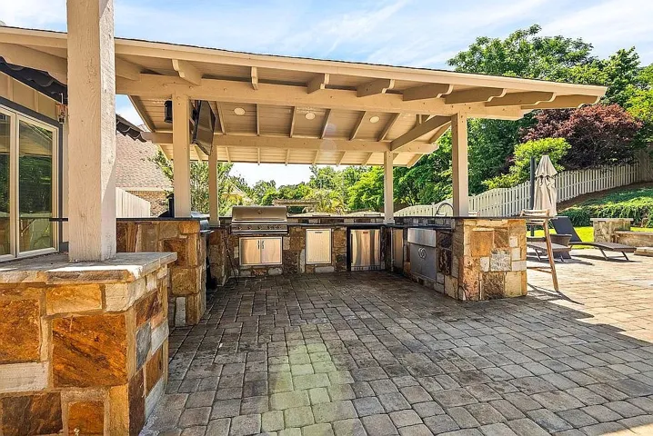 An inviting outdoor kitchen and entertaining area awaits with stone-clad appliances under a charming pergola.