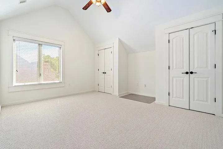 A spacious room features a vaulted ceiling, soft carpet, and a broad window for ample natural light.