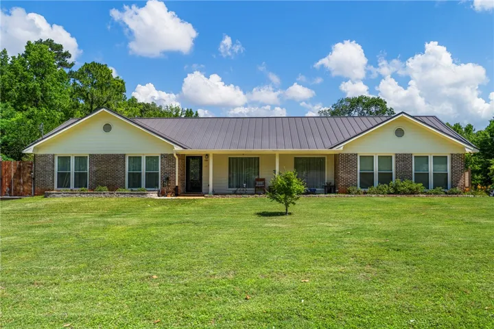 A sprawling ranch-style home features an inviting porch, brick facade, and an expansive front lawn.