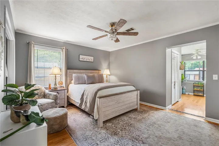 A well-lit bedroom features hardwood floors, a large window, and a charming ceiling fan.