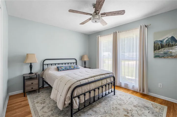 Well-lit sleeping quarters with a ceiling fan, hardwood floors, and large windows inviting ample daylight.
