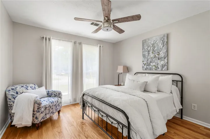 Sun-filled bedroom featuring hardwood flooring and a stylish ceiling fan for year-round comfort.