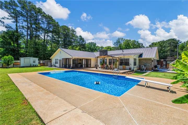 A spacious backyard oasis features an inviting in-ground pool and ample concrete patio space, perfect for outdoor enjoyment.