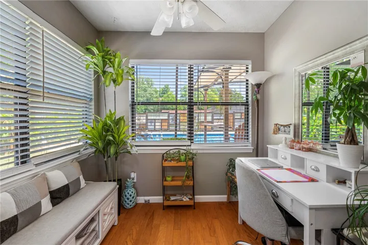 An inviting study with polished hardwood floors provides a serene workspace, offering views of the inviting pool through sun-filtering blinds.
