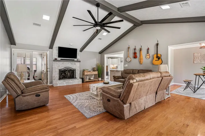 An inviting family room boasts high vaulted ceilings with exposed beams and a charming stone fireplace.