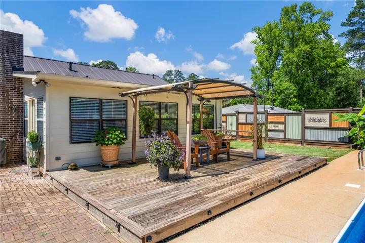A spacious wooden deck with a covered pergola offers an ideal outdoor living space, complementing the verdant yard and colorful privacy fence.
