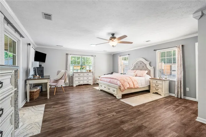 Hardwood-style flooring and multiple windows illuminate this generously sized sleeping area, ideal for peaceful slumber.