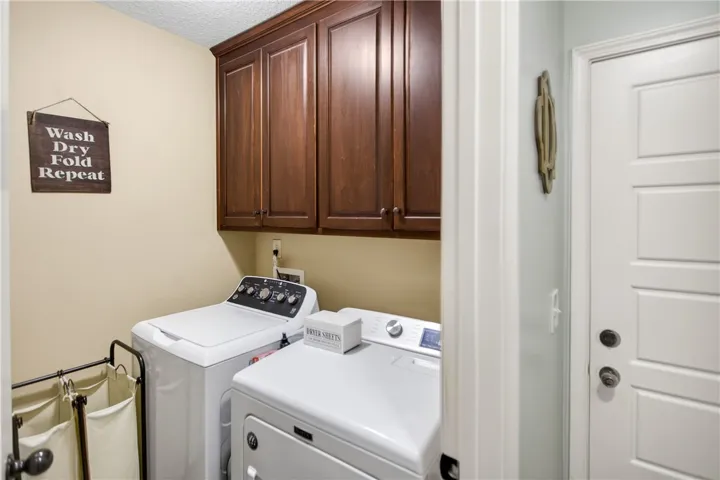 Streamlined laundry area with convenient upper cabinetry and modern appliances.