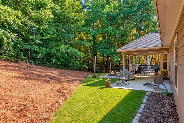 An inviting outdoor living space features a covered patio, fire pit, and ample yard backing to mature trees.