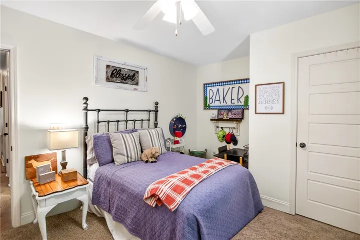 A comforting bedroom features a ceiling fan, plush carpet, and a paneled interior door.