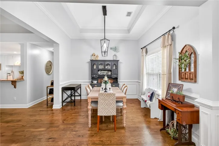 Elegant tray ceilings crown a dining area with warm hardwood flooring.