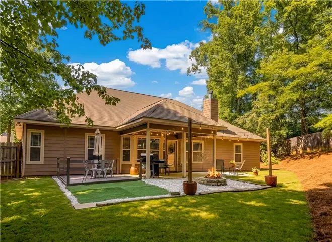 A spacious backyard features a covered patio with string lights, a deck, and a fire pit, perfect for outdoor entertaining.