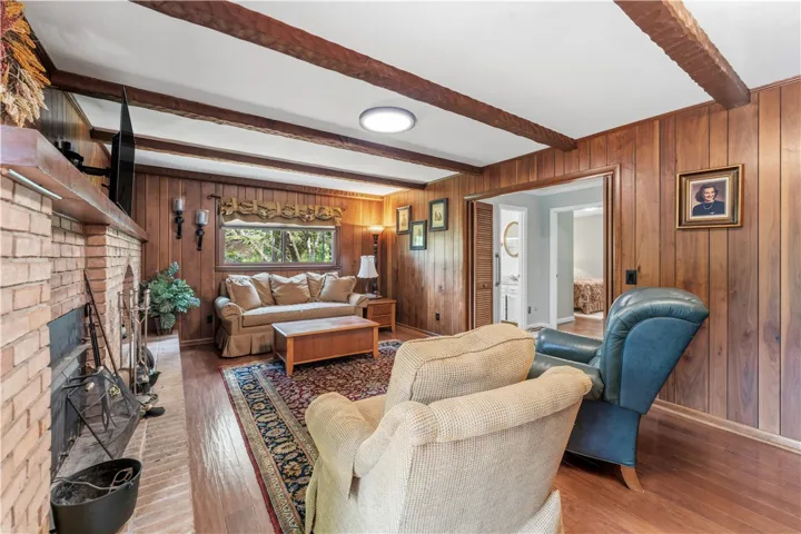 A cozy living space features warm wood paneling and exposed ceiling beams, centered around a brick fireplace.