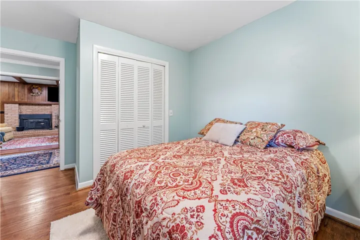 Hardwood flooring extends from this comfortable bedroom into an adjacent living space with a classic brick fireplace.