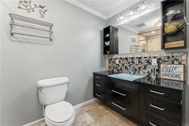 An inviting full bath featuring a glass basin, tile flooring, and a decorative tile backsplash.