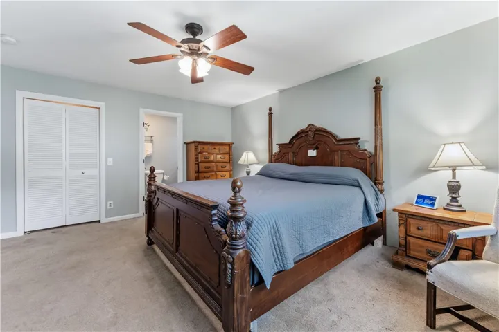 A comfortable bedroom features a ceiling fan, plush carpet, and a convenient closet.