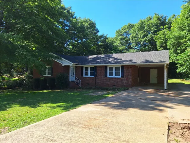 Mature trees frame this classic brick facade with a welcoming front entry and convenient carport.