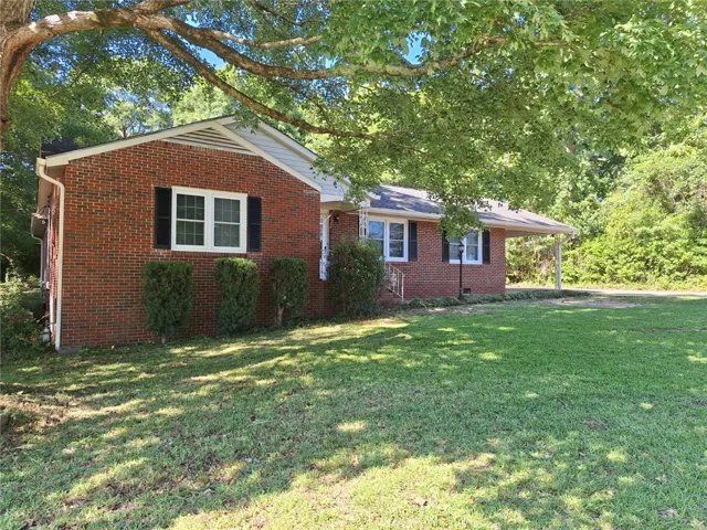 A well-maintained brick residence is framed by mature trees, offering ample green space and a welcoming front facade.