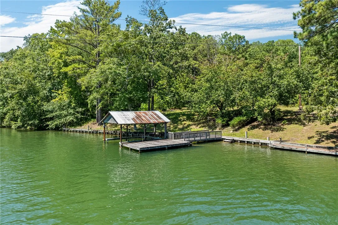 A tranquil lake view featuring a private dock and a mature tree-lined shore.
