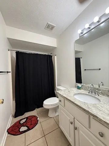 Well-lit bathroom with a vanity, tiled flooring, and essential fixtures.